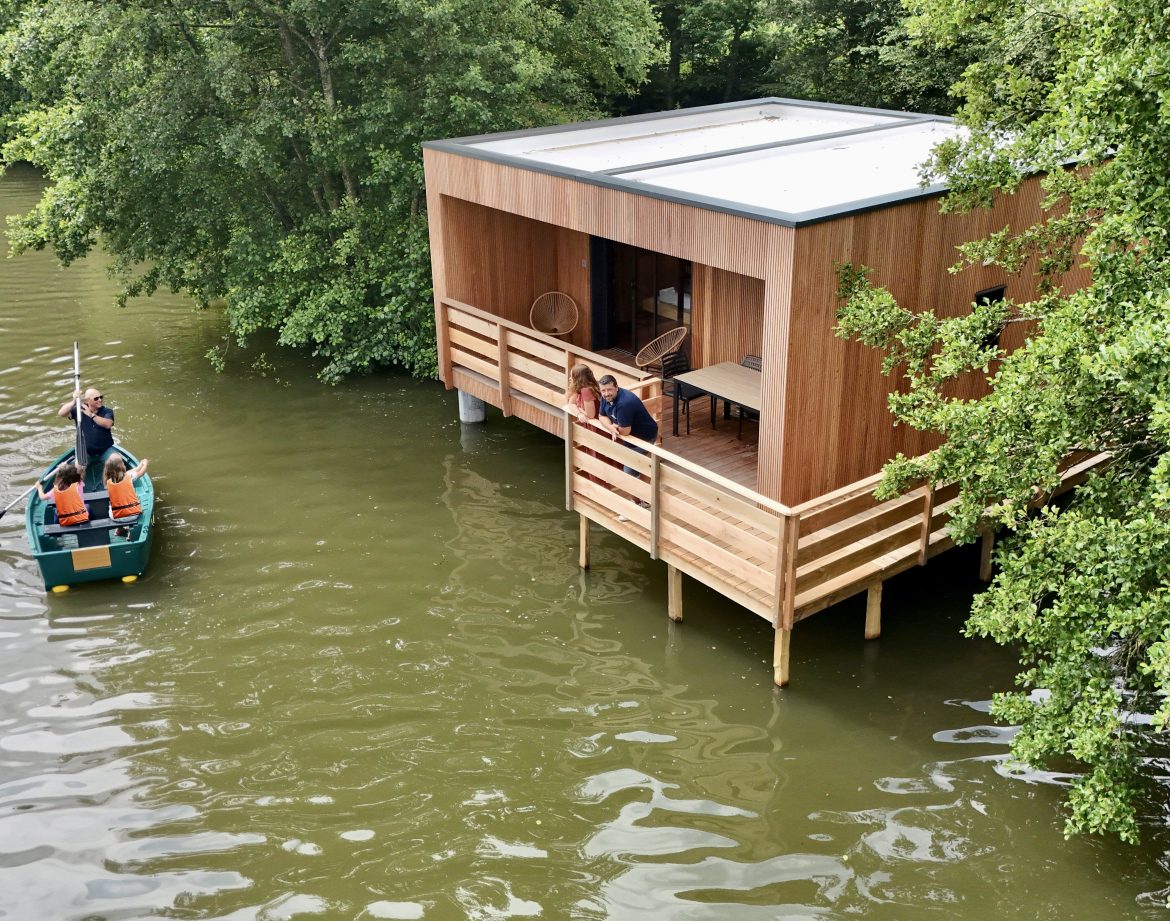 Cabane sur pilotis au bord de l'eau, entourée de verdure, avec un accès en bateau.