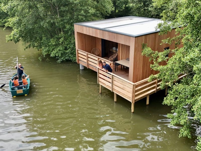 Cabane sur pilotis au bord de l'eau, entourée de verdure, avec un accès en bateau.