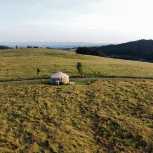 Yourte isolée au milieu des champs verdoyants, offrant une vue panoramique sur les collines.