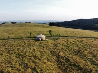 Yourte isolée au milieu des champs verdoyants, offrant une vue panoramique sur les collines.