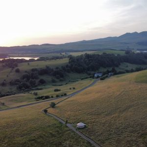 Yourte isolée au cœur d'un paysage verdoyant, avec des collines et un lac en arrière-plan.