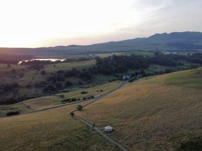 Yourte isolée au cœur d'un paysage verdoyant, avec des collines et un lac en arrière-plan.