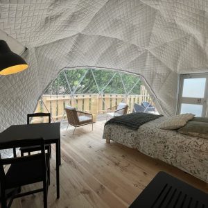 Dôme géodésique lumineux avec lit douillet et vue sur la nature, ambiance moderne et chaleureuse.
