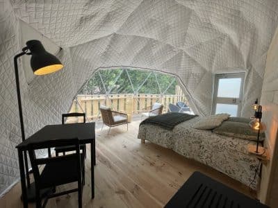 Dôme géodésique lumineux avec lit douillet et vue sur la nature, ambiance moderne et chaleureuse.