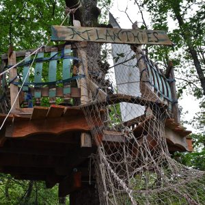 Cabane perchée dans les arbres, décorée de bois et de filets, offrant une vue imprenable sur la