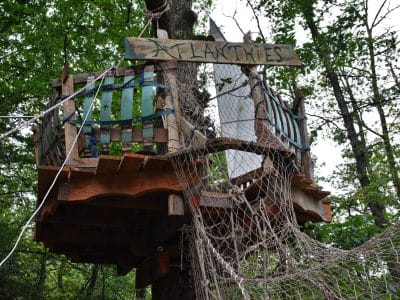 Cabane perchée dans les arbres, décorée de bois et de filets, offrant une vue imprenable sur la