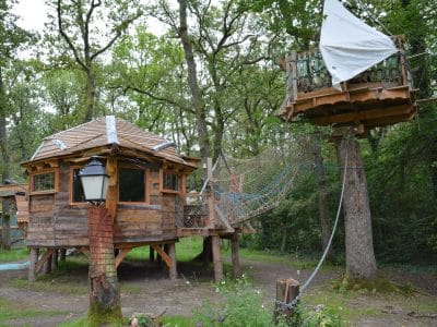 Cabane en bois perchée dans les arbres, avec un pont suspendu et une décoration rustique.