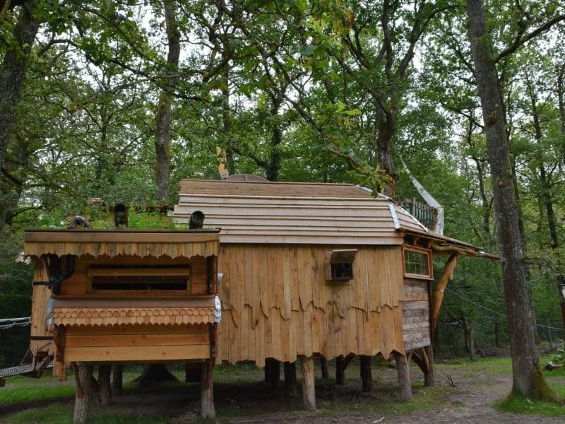 Cabane en bois perchée dans les arbres, entourée de verdure luxuriante. Un hébergement insolite.