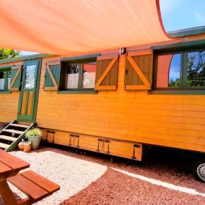 Charmante roulotte en bois avec volets colorés, située dans un cadre verdoyant.