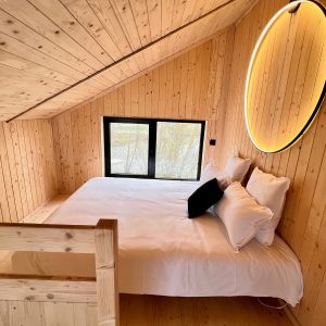 Chalet en bois chaleureux avec lit douillet et grande fenêtre offrant une vue apaisante.