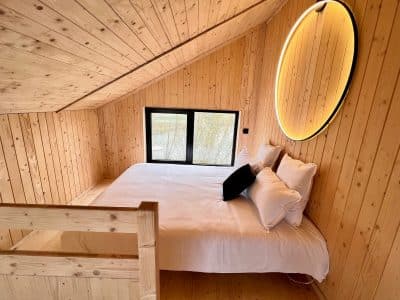 Chalet en bois chaleureux avec lit douillet et grande fenêtre offrant une vue apaisante.