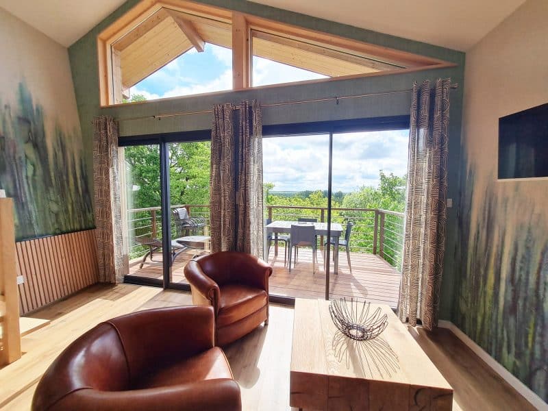 Chalet moderne avec grandes baies vitrées et vue sur la nature verdoyante.