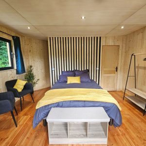 Chalet en bois moderne avec lit douillet, touches de jaune et vue sur la nature.