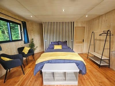 Chalet en bois moderne avec lit douillet, touches de jaune et vue sur la nature.