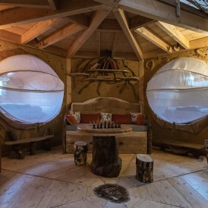 Cabane en bois avec de grandes fenêtres rondes, décorée de meubles naturels et chaleureux.