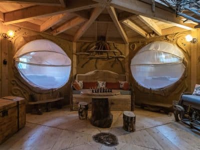 Cabane en bois avec de grandes fenêtres rondes, décorée de meubles naturels et chaleureux.