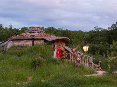 Hébergement insolite : une maison en bois au toit végétal, entourée de verdure et d'une lampe