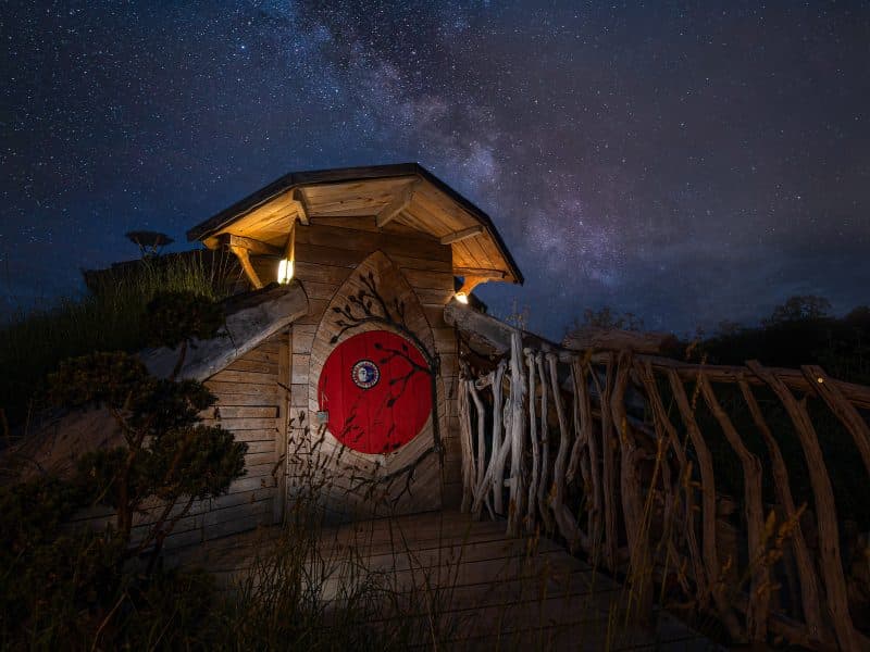 Cabane en bois avec une porte rouge, sous un ciel étoilé magnifique.