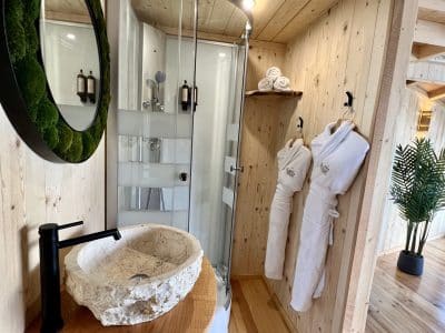 Salle de bain d'un hébergement insolite en bois, avec douche moderne et lavabo en pierre.