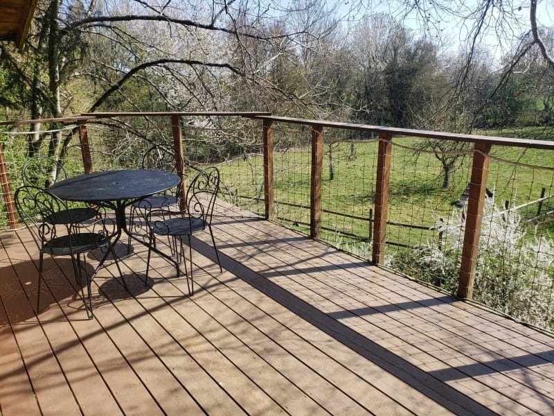 Chalet en bois avec terrasse ensoleillée et vue sur un jardin verdoyant.