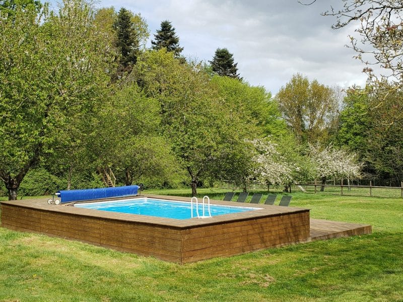 Maison de vacances avec piscine entourée dun jardin verdoyant et darbres.