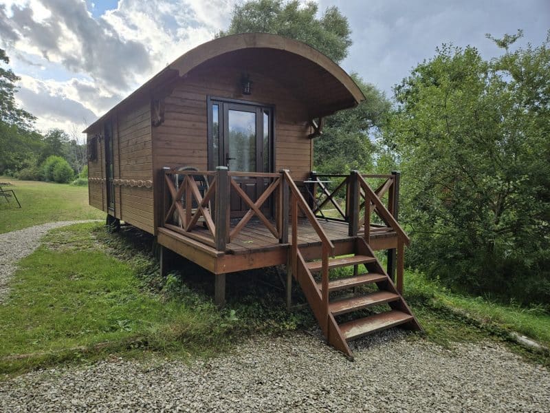 Chalet en bois avec terrasse, entouré de verdure et ciel nuageux.