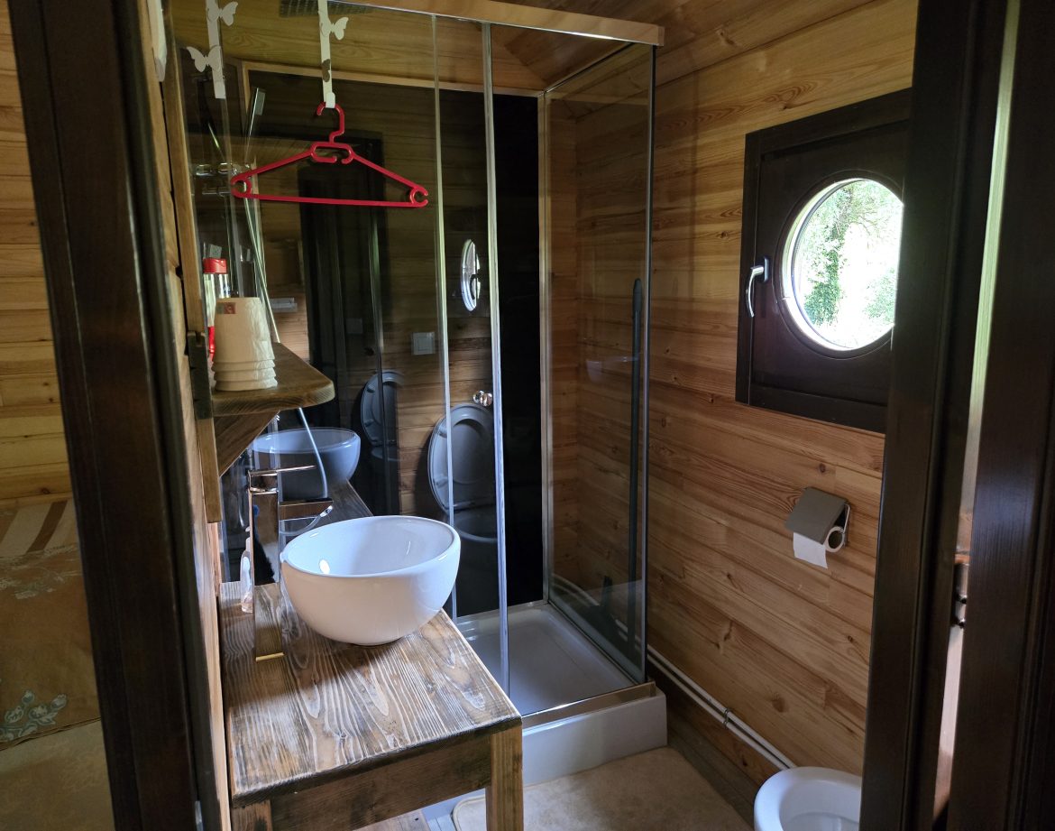 Salle de bain en bois dans un hébergement insolite, avec douche vitrée et lavabo moderne.