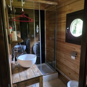 Salle de bain en bois dans un hébergement insolite, avec douche vitrée et lavabo moderne.