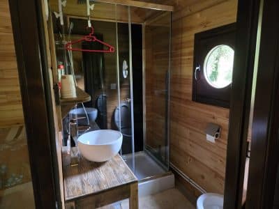 Salle de bain en bois dans un hébergement insolite, avec douche vitrée et lavabo moderne.