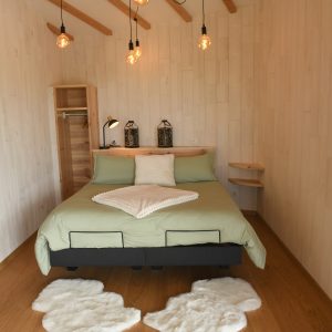 Chambre moderne en bois avec lit douillet et éclairage suspendu, ambiance chaleureuse.