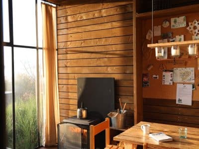 Cabane en bois chaleureuse avec cheminée, grandes fenêtres et mobilier en bois naturel.