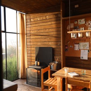 Un chalet en bois chaleureux avec un poêle, des chaises en bois et une vue sur la nature.