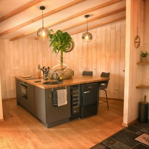 Cuisine moderne dans un chalet en bois, avec un îlot central et des luminaires suspendus.