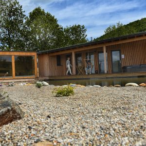 Cabane en bois moderne avec terrasse, entourée de galets et de verdure apaisante.