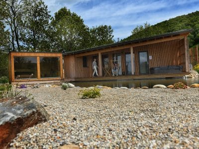 Cabane en bois moderne avec terrasse, entourée de galets et de verdure apaisante.