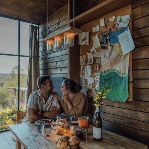 Un chalet en bois chaleureux, avec une grande table, des lumières suspendues et une vue apaisante.
