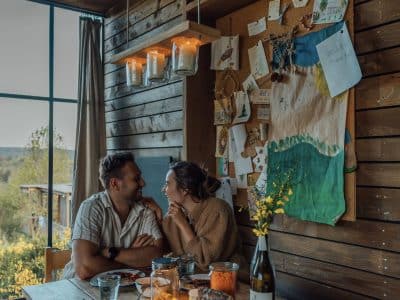 Un chalet en bois chaleureux, avec une grande table, des lumières suspendues et une vue apaisante.