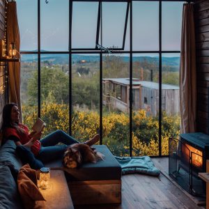 Cabane moderne avec grandes fenêtres, vue sur la nature, ambiance chaleureuse et cosy.