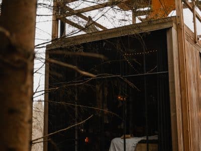 Cabane suspendue dans les arbres, avec de grandes fenêtres offrant une vue sur la forêt.