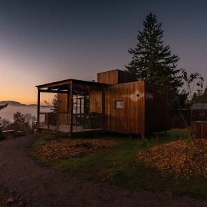 Cabane en bois moderne, perchée sur une colline avec vue sur un paysage brumeux au coucher du