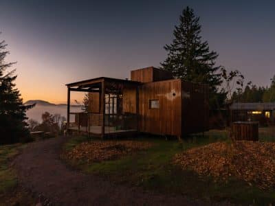 Cabane en bois moderne, perchée sur une colline avec vue sur un paysage brumeux au coucher du