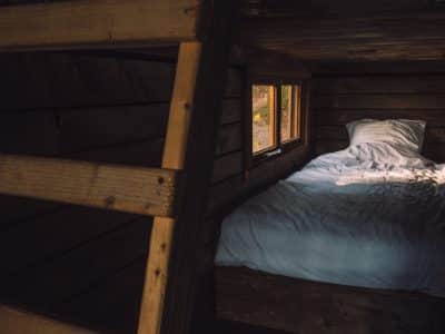 Cabane en bois avec un lit douillet et des fenêtres laissant entrer la lumière naturelle.