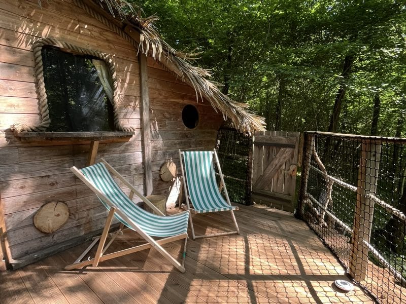 Cabane dans les arbres avec chaises longues sur une terrasse en bois, entourée de verdure.