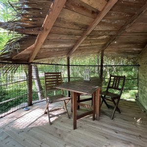 Cabane perchée dans les arbres, avec une table en bois et des chaises, entourée de verdure.