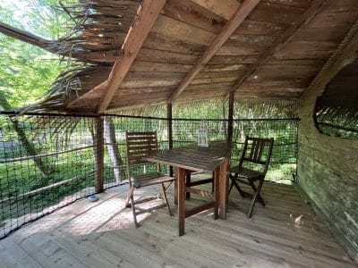 Cabane perchée dans les arbres, avec une table en bois et des chaises, entourée de verdure.