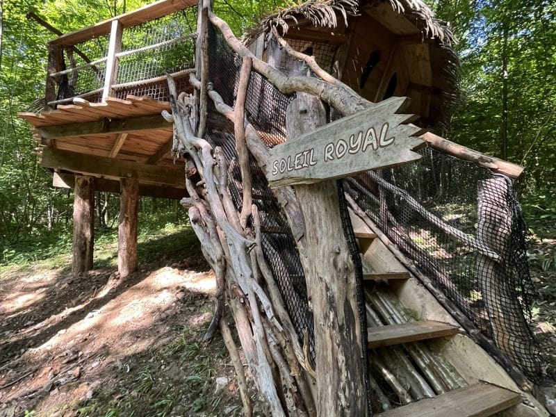 Cabane perchée dans les arbres, avec un accès en bois et une ambiance naturelle.