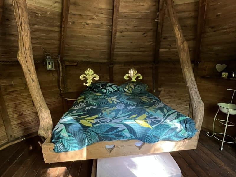 Chalet en bois avec lit suspendu et décor tropical, ambiance chaleureuse et unique.