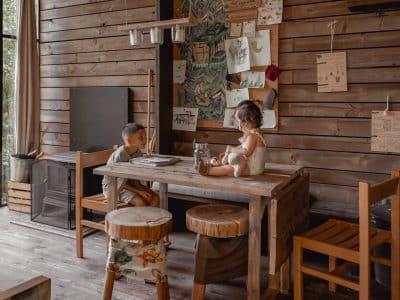 Intérieur chaleureux d'un chalet en bois, enfants assis à une table rustique, ambiance conviviale.