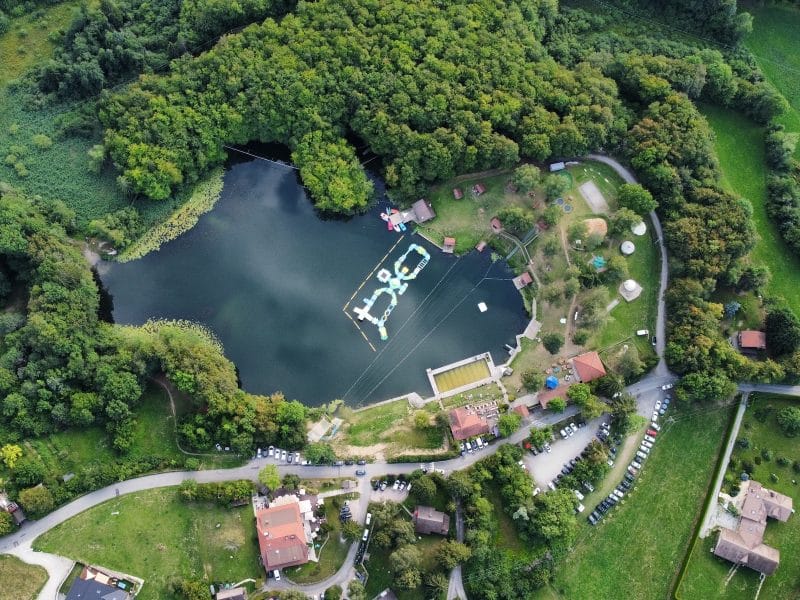 Vue aérienne dun camping au bord dun lac, entouré de verdure luxuriante.