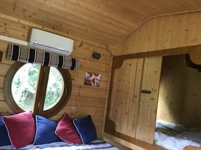 Cabane en bois avec fenêtres rondes, décor chaleureux et coussins colorés pour un séjour cosy.